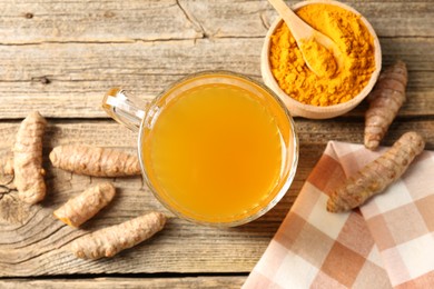 Photo of Aromatic turmeric tea in glass mug, roots and powder on wooden table, flat lay