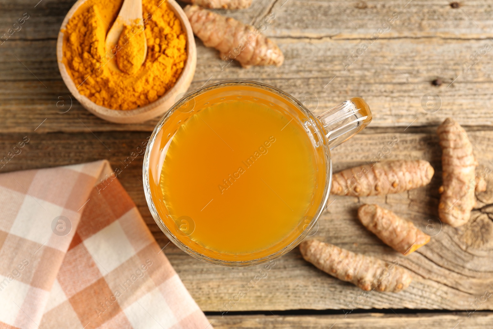 Photo of Aromatic turmeric tea in glass mug, roots and powder on wooden table, flat lay