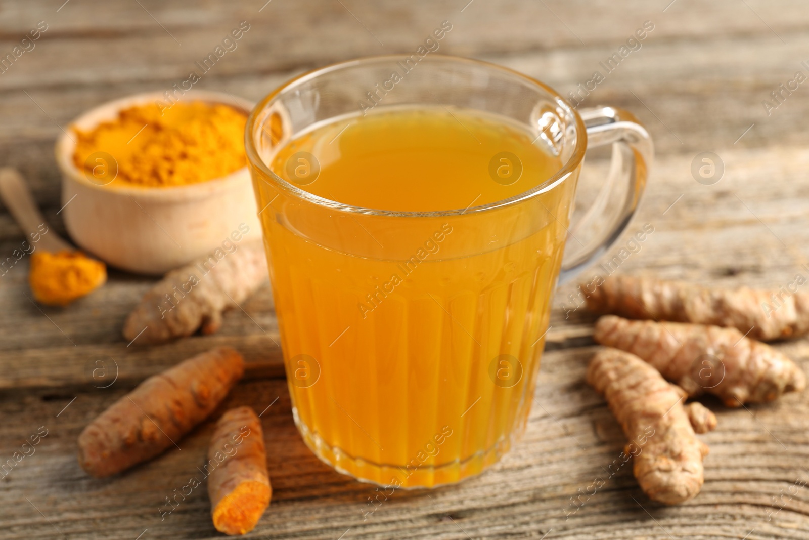 Photo of Aromatic turmeric tea in glass mug, roots and powder on wooden table, closeup