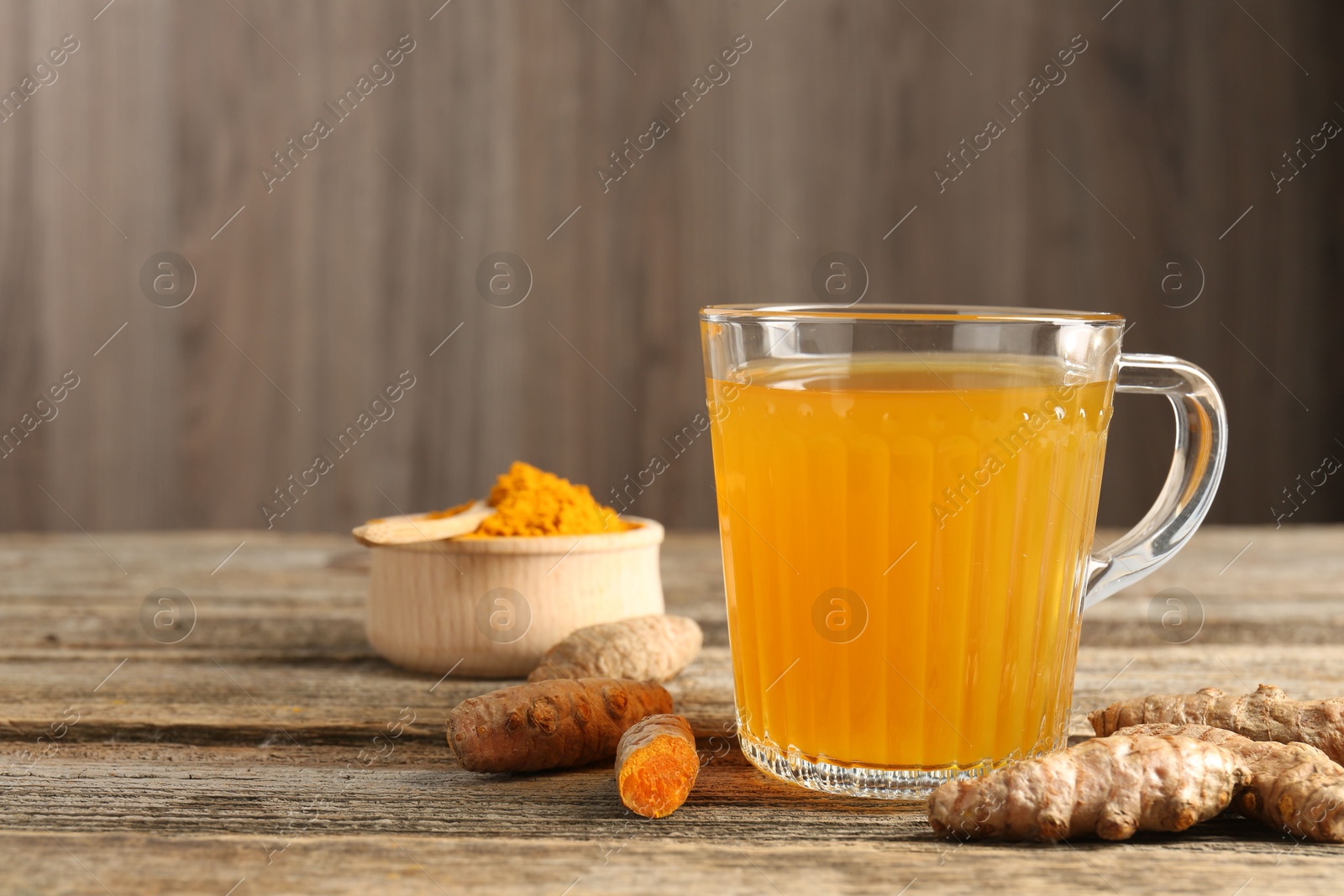 Photo of Aromatic turmeric tea in glass mug, roots and powder on wooden table, space for text