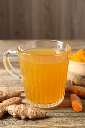 Photo of Aromatic turmeric tea in glass mug, roots and powder on wooden table, closeup