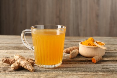 Photo of Aromatic turmeric tea in glass mug, roots and powder on wooden table