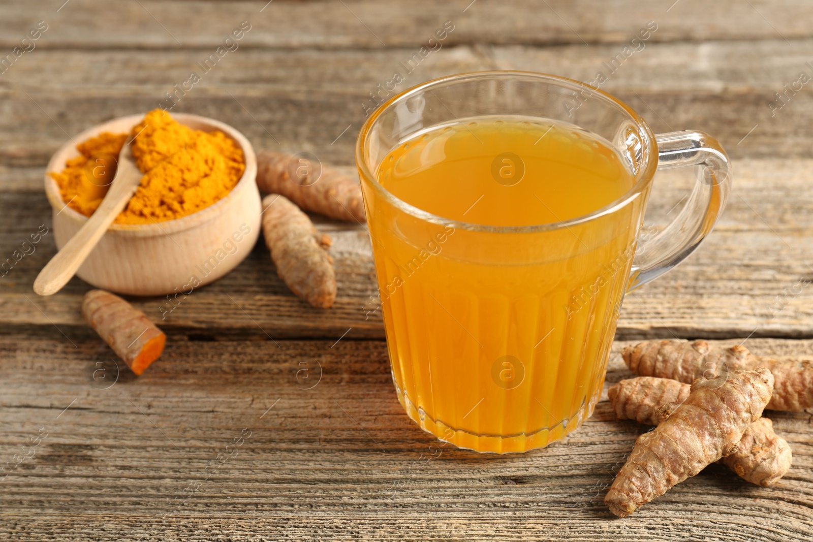 Photo of Aromatic turmeric tea in glass mug, roots and powder on wooden table, closeup