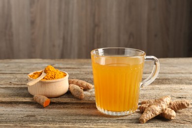 Photo of Aromatic turmeric tea in glass mug, roots and powder on wooden table