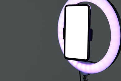 Photo of Ring lamp with smartphone on grey background, closeup. Space for text