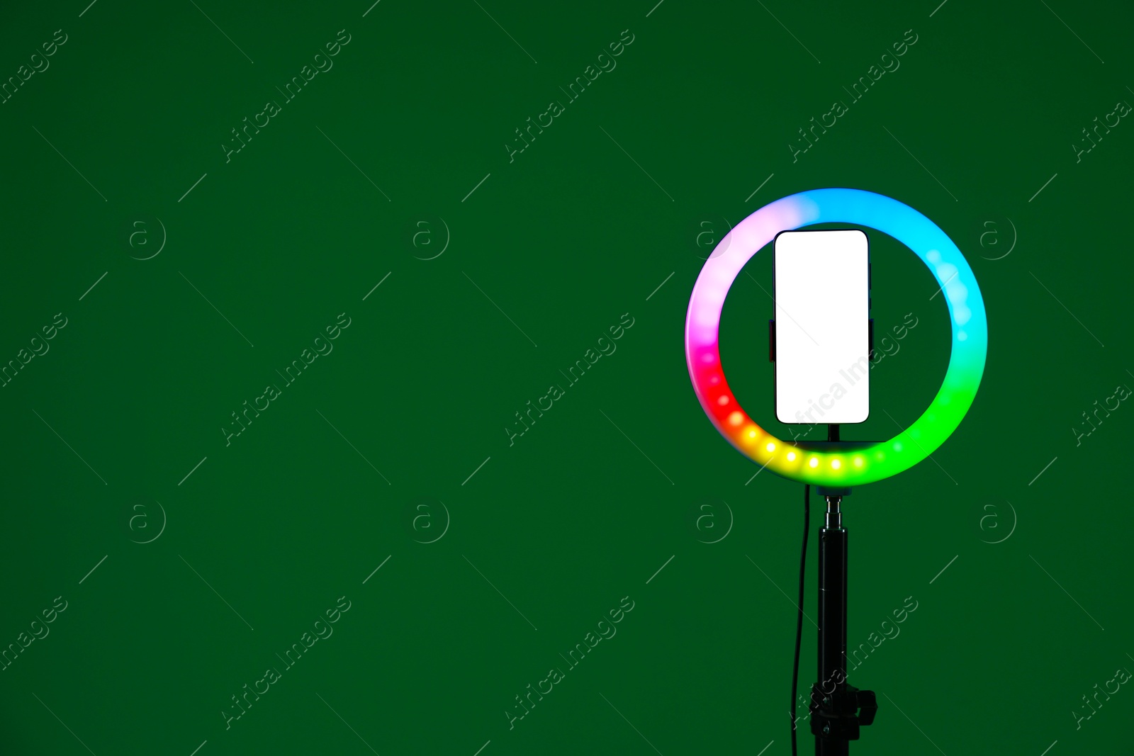 Photo of Ring lamp with smartphone on green background, space for text