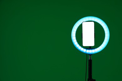 Photo of Ring lamp with smartphone on green background, space for text