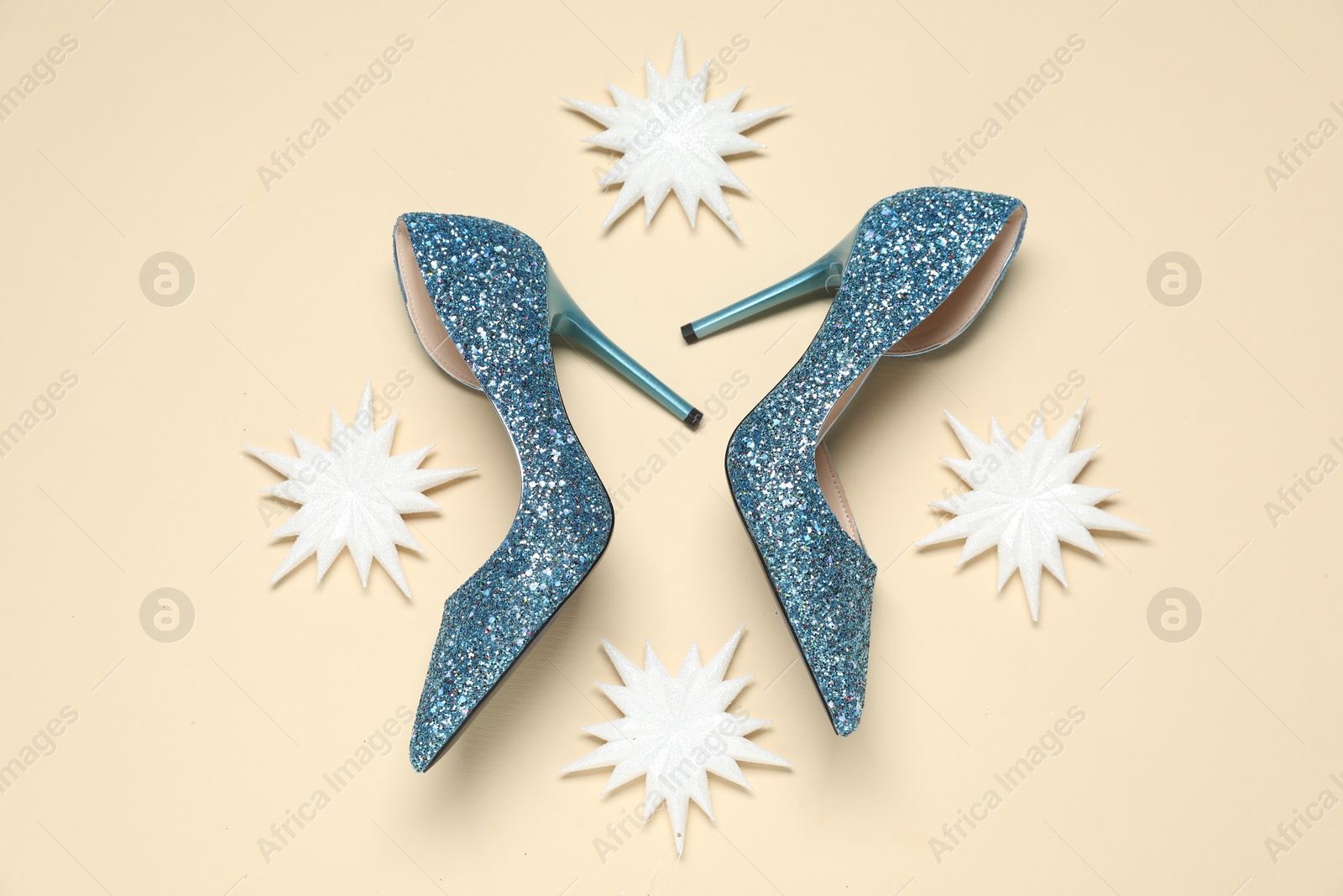 Photo of Shiny high heeled shoes and decorative snowflakes on beige background, flat lay