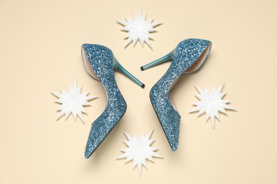 Shiny high heeled shoes and decorative snowflakes on beige background, flat lay