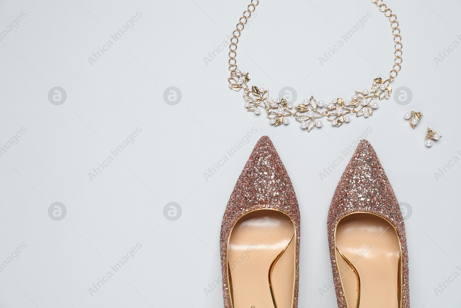 Photo of Shiny high heeled shoes and accessories on light grey background, flat lay. Space for text