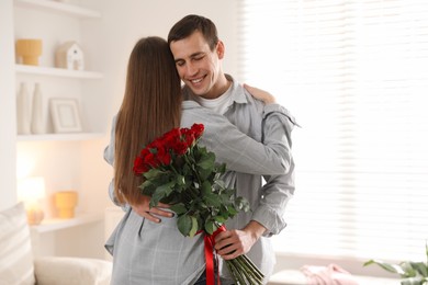 Photo of Lovely couple with bouquet of red roses indoors. Valentine's day celebration