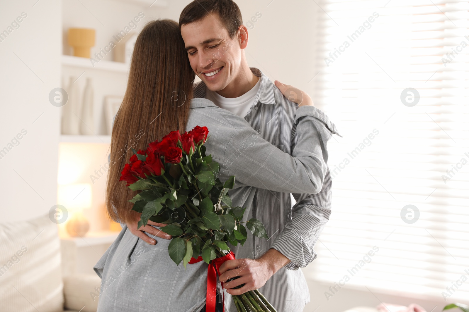 Photo of Lovely couple with bouquet of red roses indoors. Valentine's day celebration