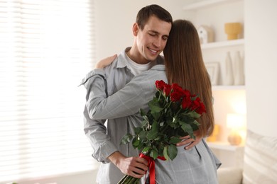 Photo of Lovely couple with bouquet of red roses indoors. Valentine's day celebration