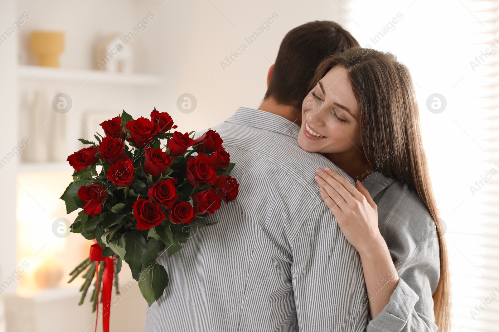 Photo of Lovely couple with bouquet of red roses indoors. Valentine's day celebration