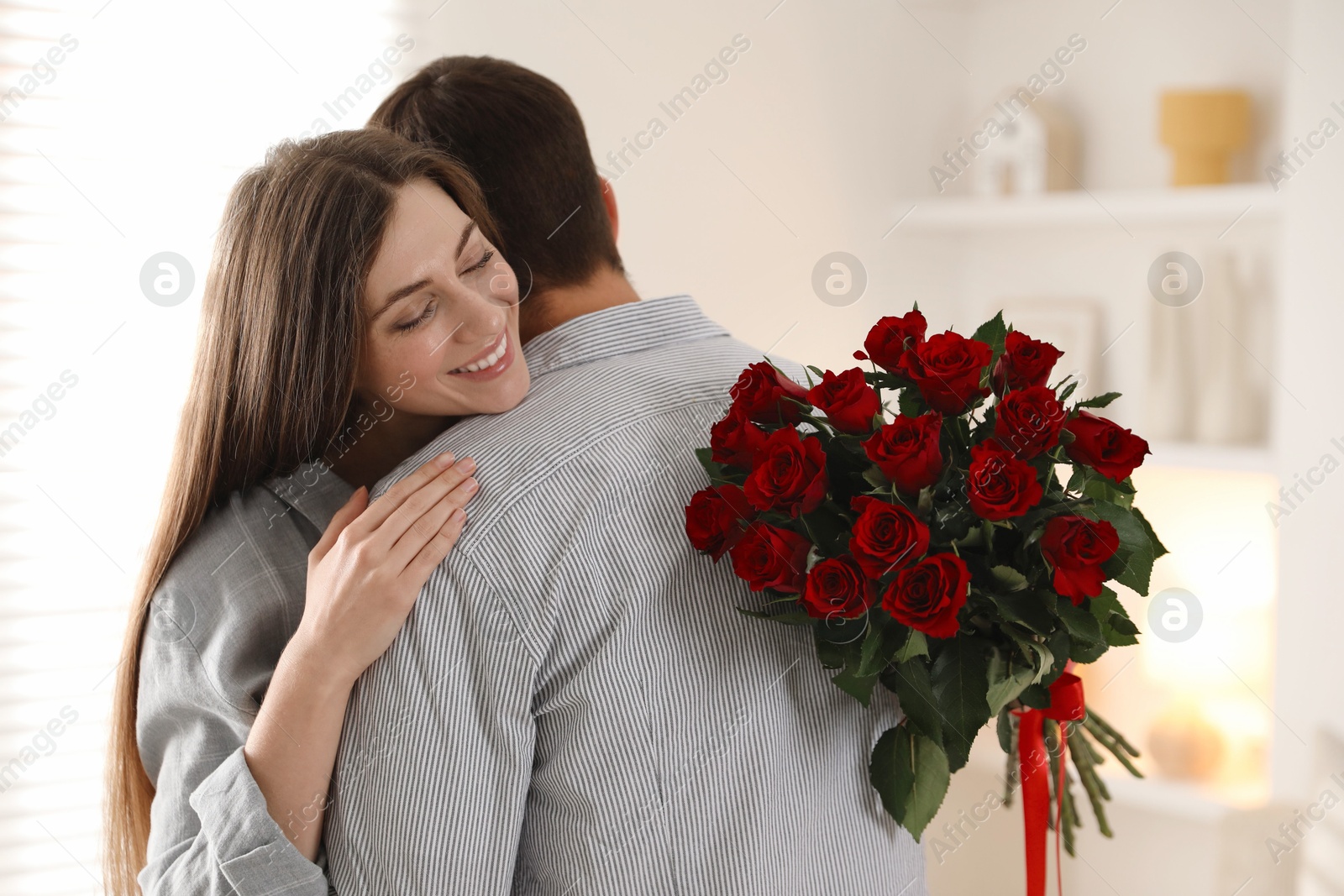 Photo of Lovely couple with bouquet of red roses indoors. Valentine's day celebration