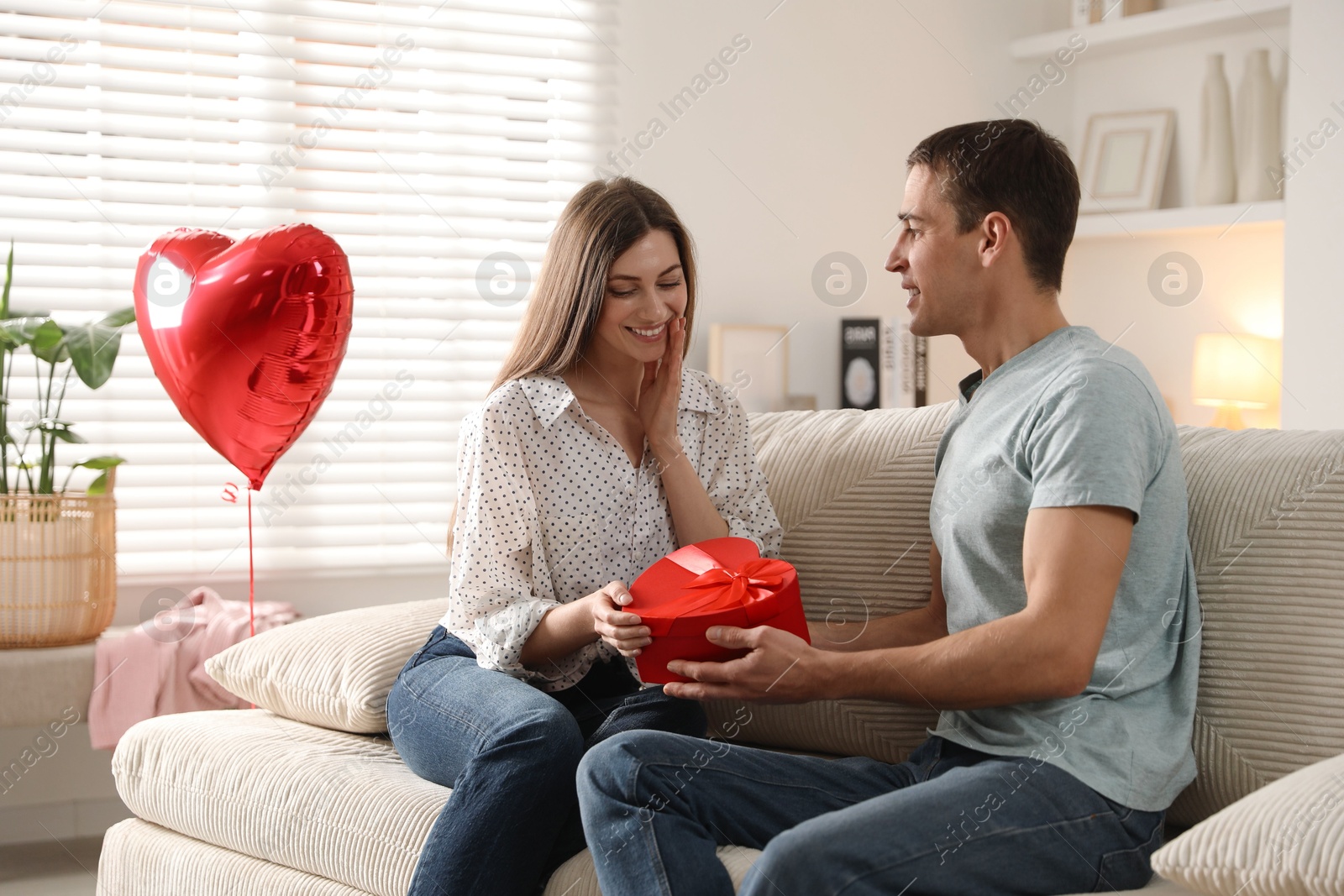 Photo of Lovely man surprising his girlfriend with Valentine's day gift indoors