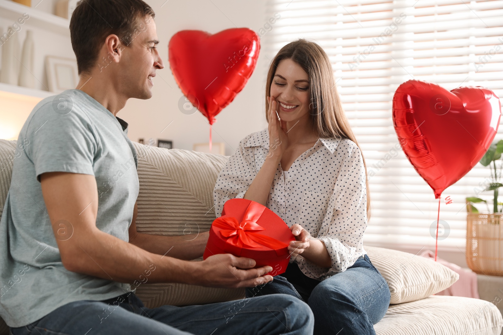 Photo of Lovely man surprising his girlfriend with Valentine's day gift indoors