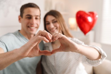 Photo of Lovely couple making heart with hands indoors, selective focus. Valentine's day celebration