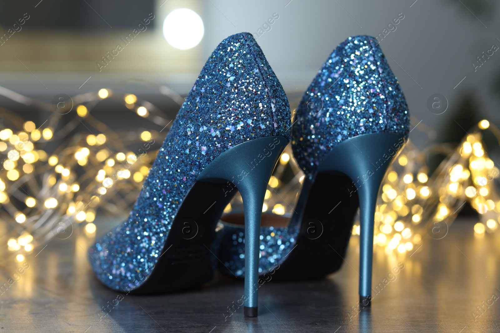 Photo of Shiny high heeled shoes and festive lights on grey table indoors, closeup