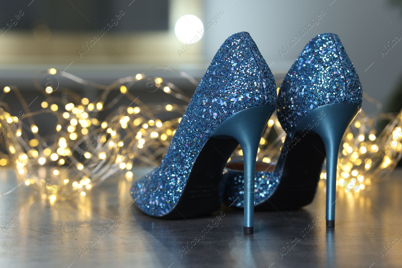 Photo of Shiny high heeled shoes and festive lights on grey table indoors, closeup