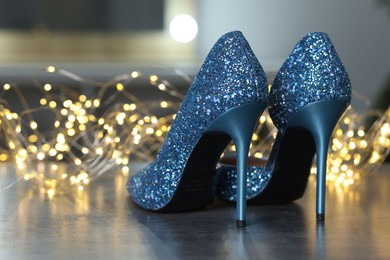 Photo of Shiny high heeled shoes and festive lights on grey table indoors, closeup