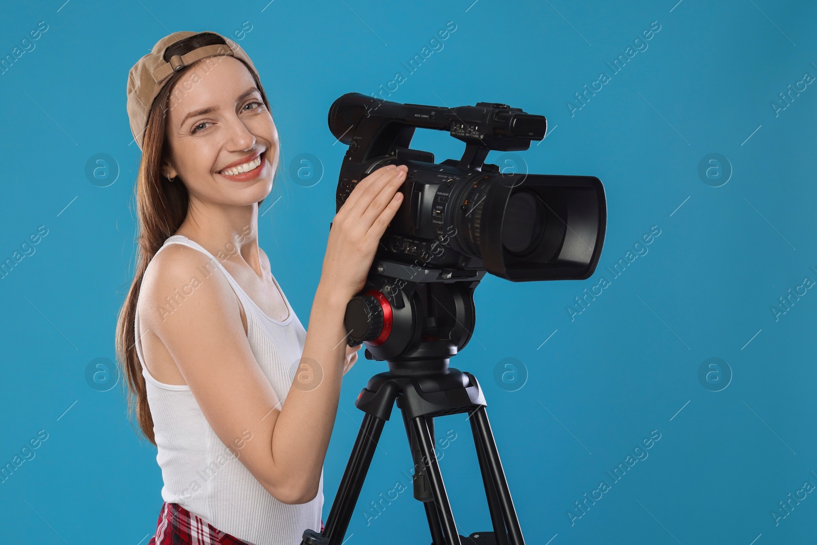 Photo of Happy woman with professional video camera on light blue background