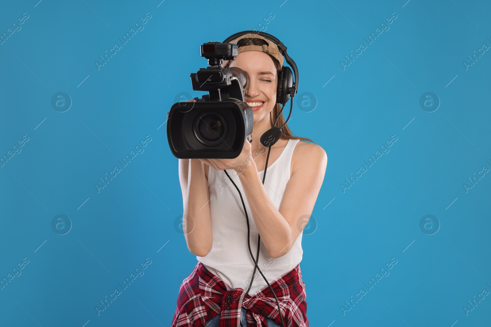 Photo of Happy woman with professional video camera and headset on light blue background