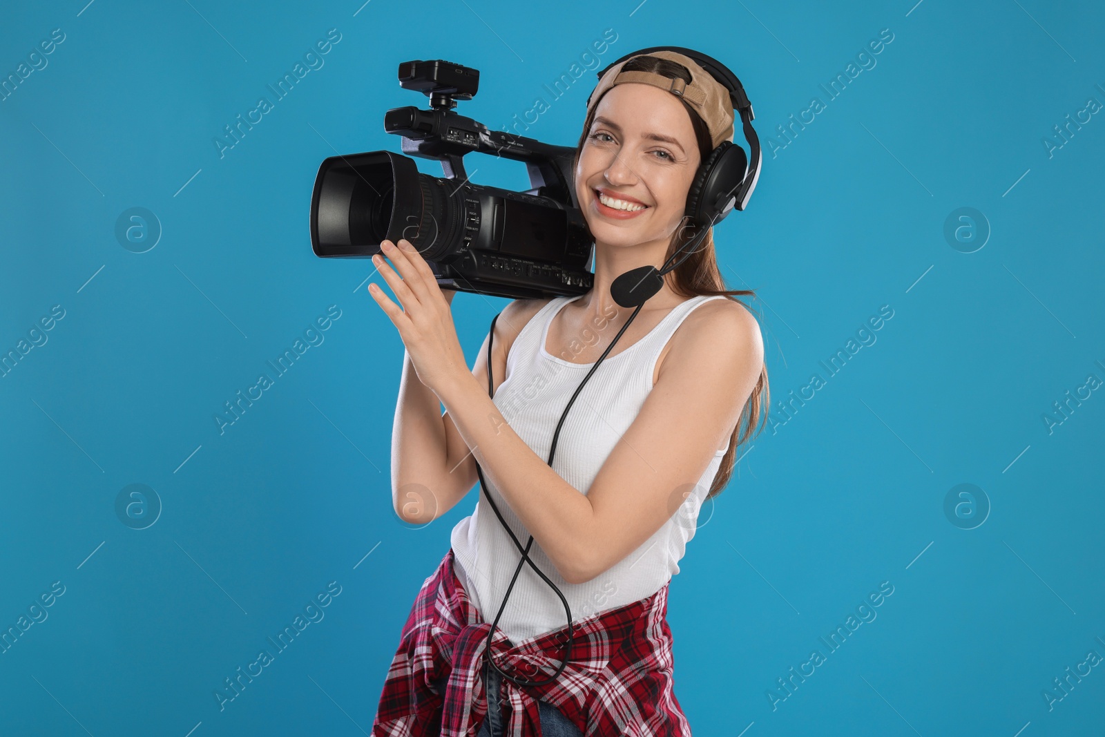 Photo of Happy woman with professional video camera and headset on light blue background