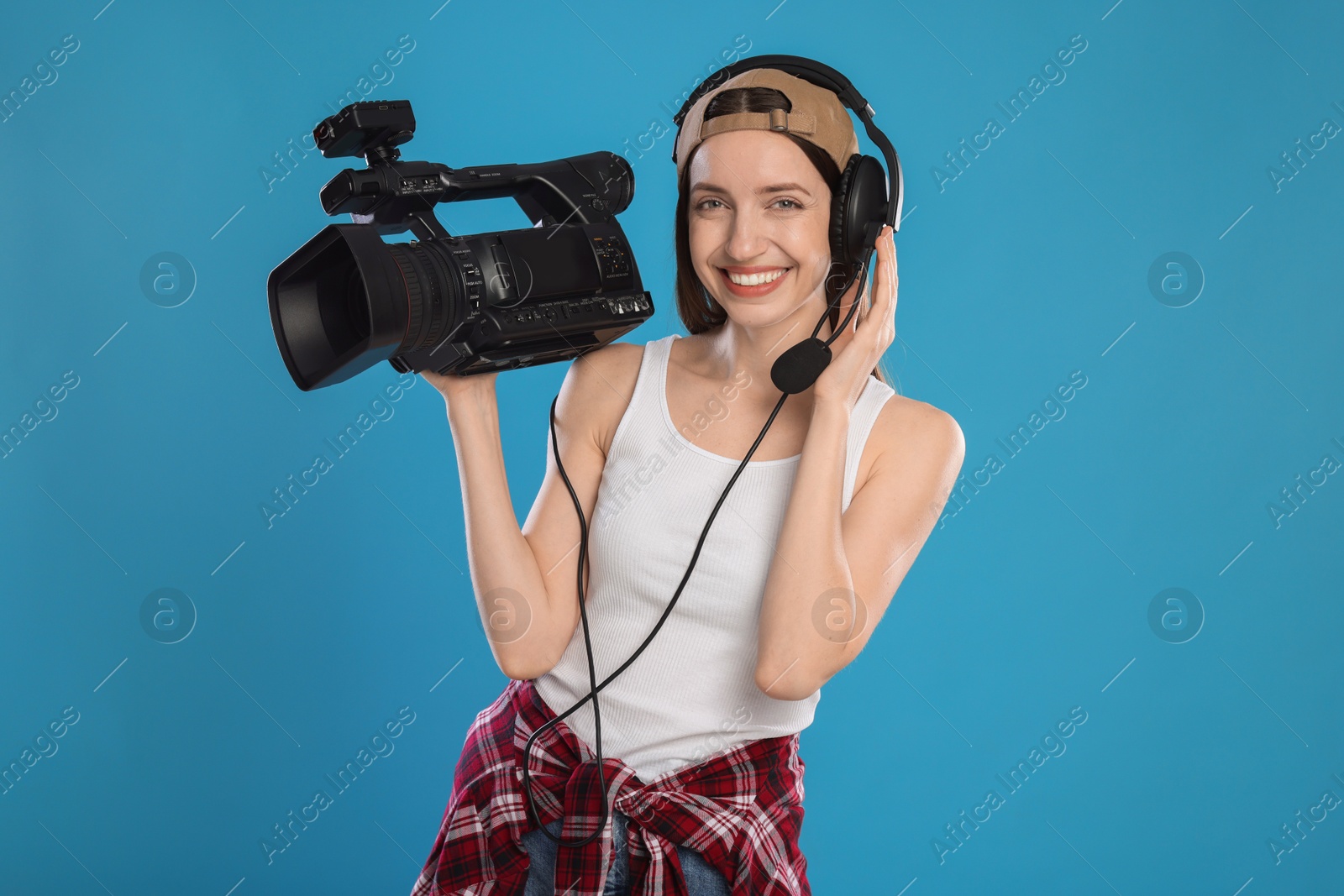 Photo of Happy woman with professional video camera and headset on light blue background