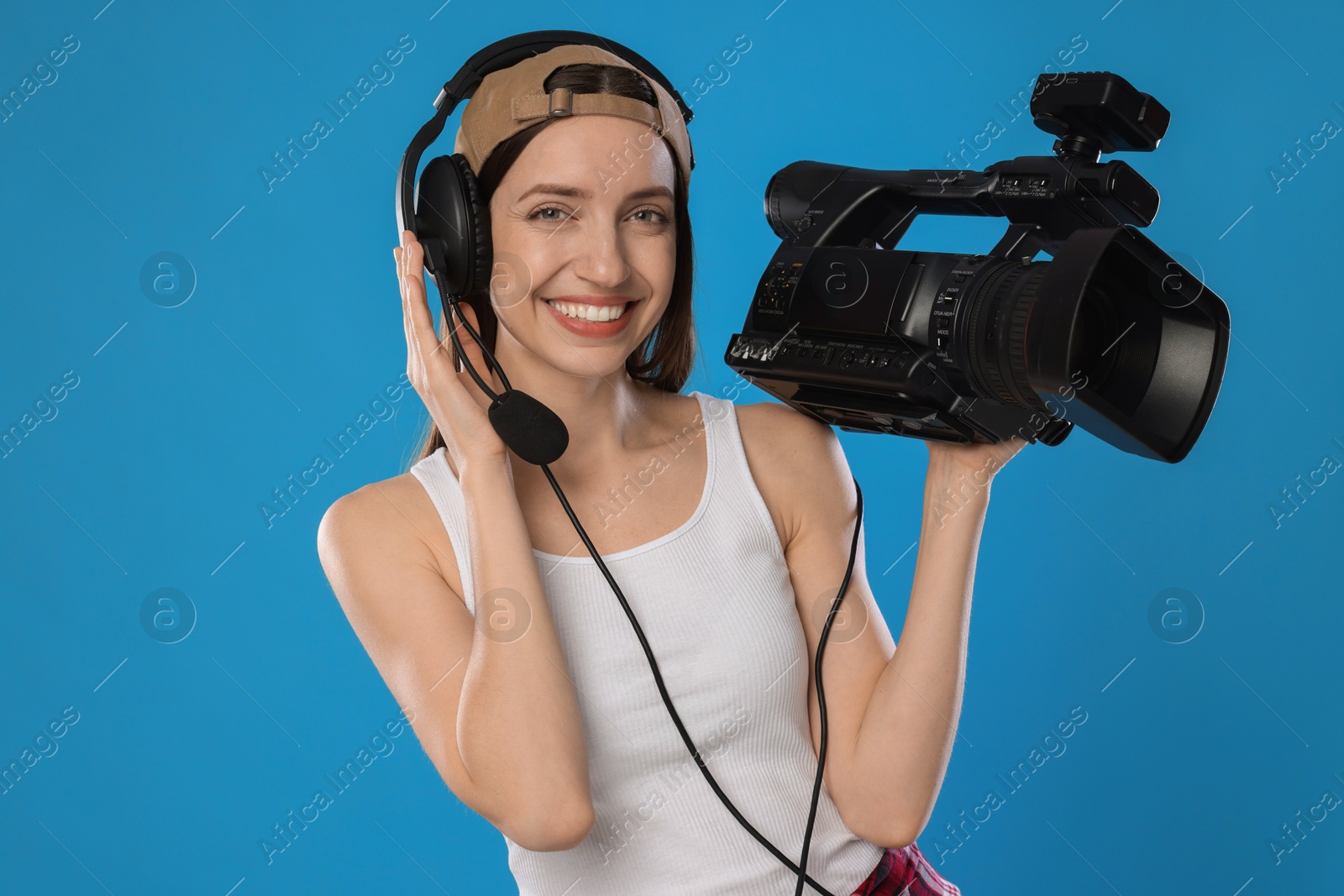 Photo of Happy woman with professional video camera and headset on light blue background