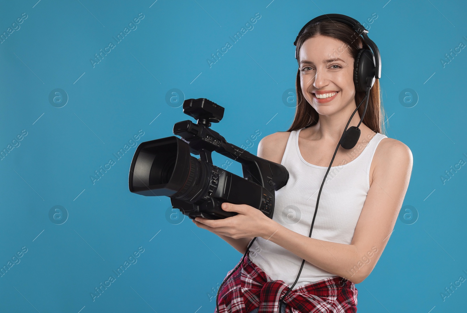 Photo of Happy woman with professional video camera and headset on light blue background, space for text