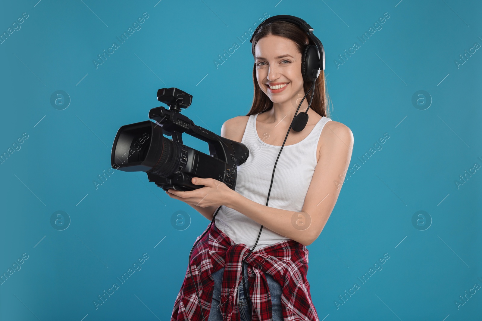 Photo of Happy woman with professional video camera and headset on light blue background