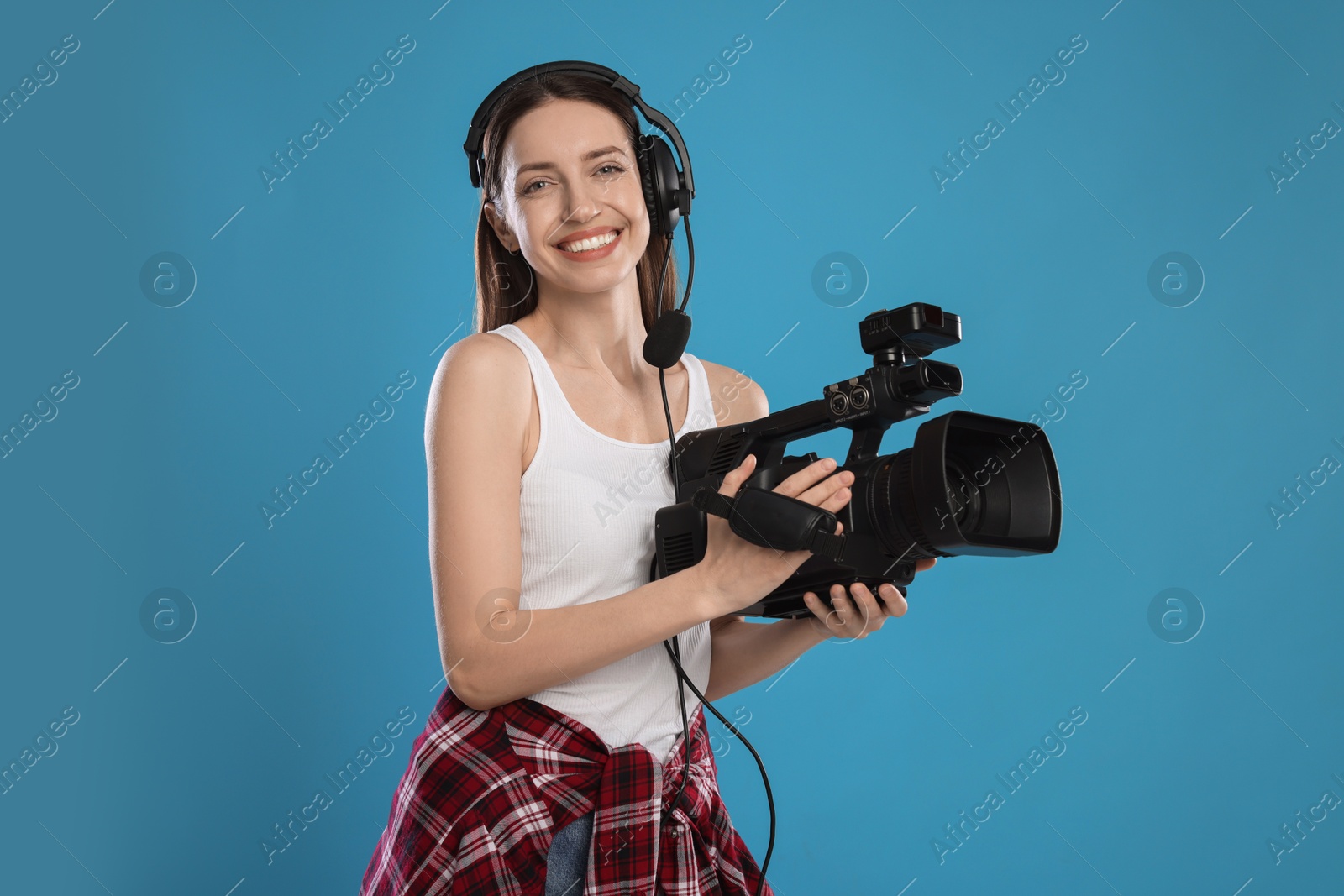 Photo of Happy woman with professional video camera and headset on light blue background