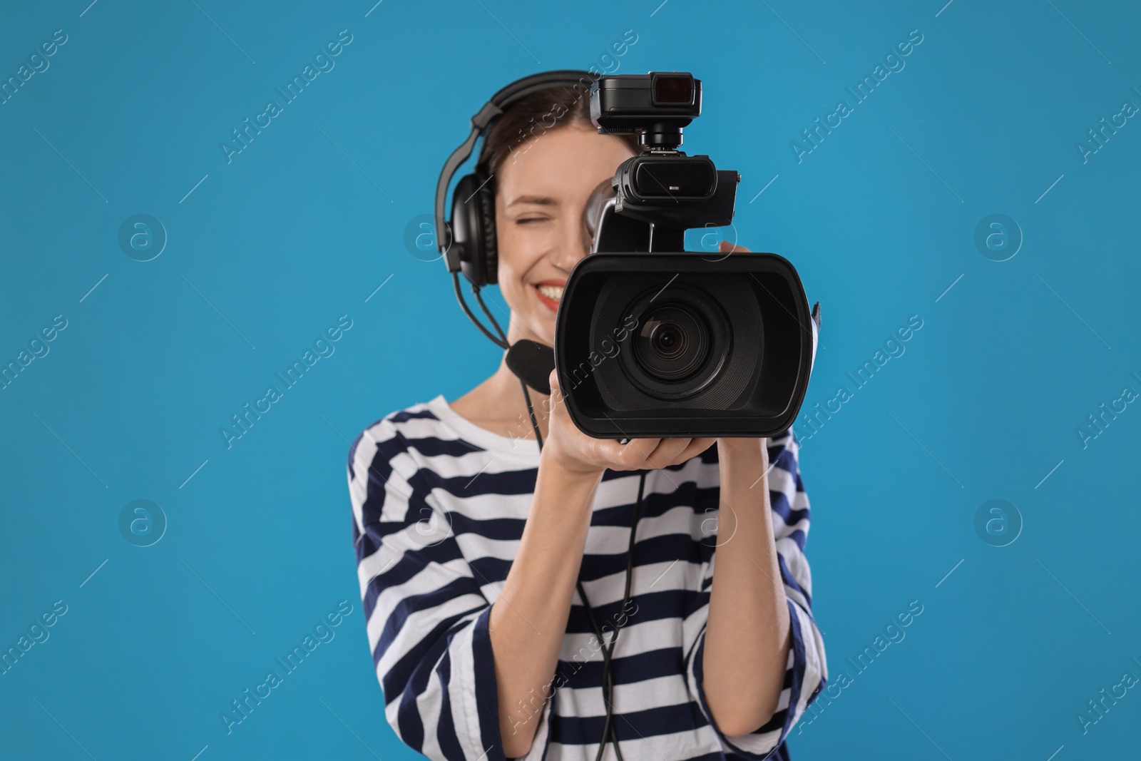 Photo of Happy woman with professional video camera and headset on light blue background, selective focus