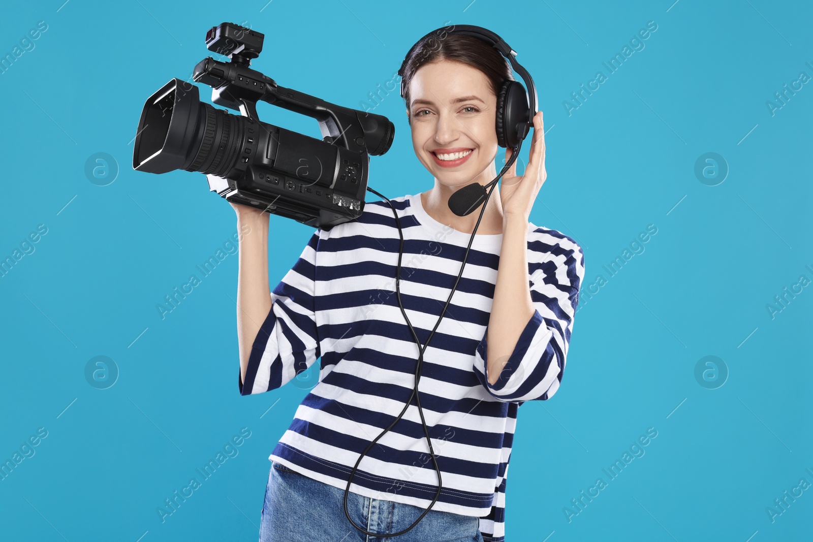 Photo of Happy woman with professional video camera and headset on light blue background