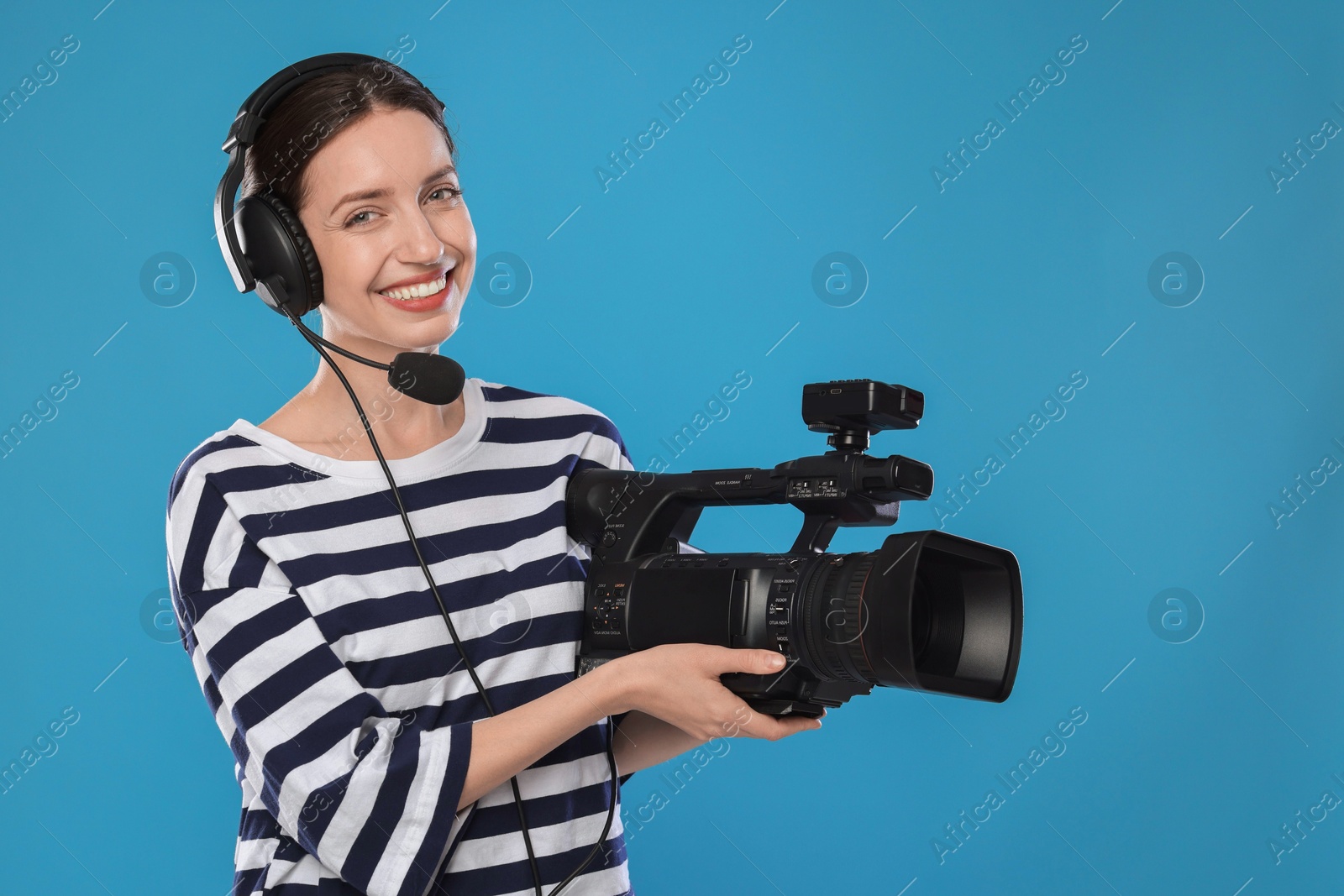 Photo of Happy woman with professional video camera and headset on light blue background