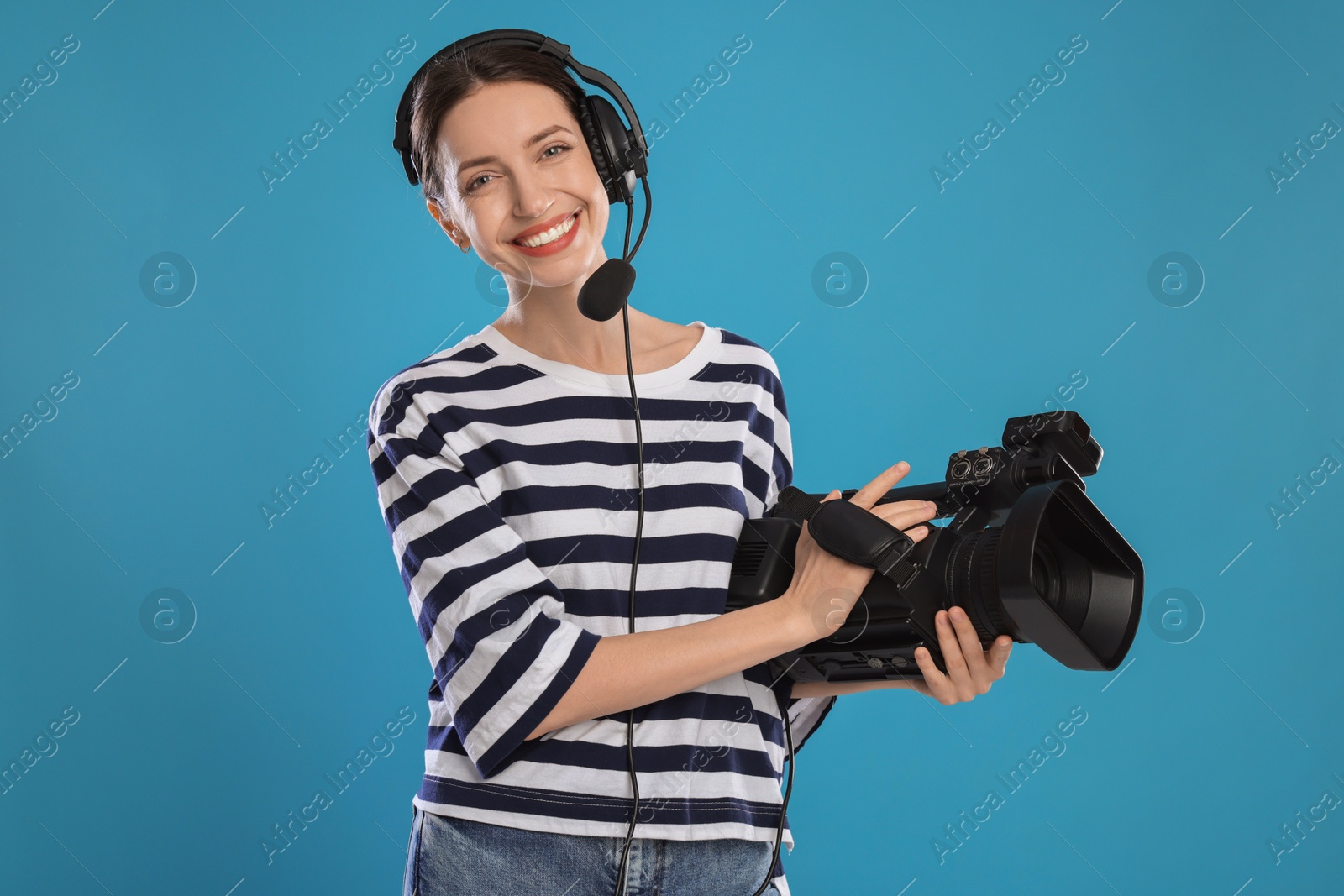 Photo of Happy woman with professional video camera and headset on light blue background