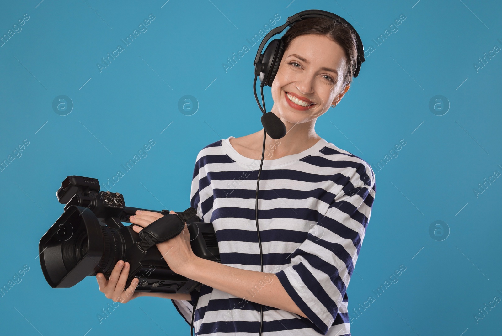 Photo of Happy woman with professional video camera and headset on light blue background