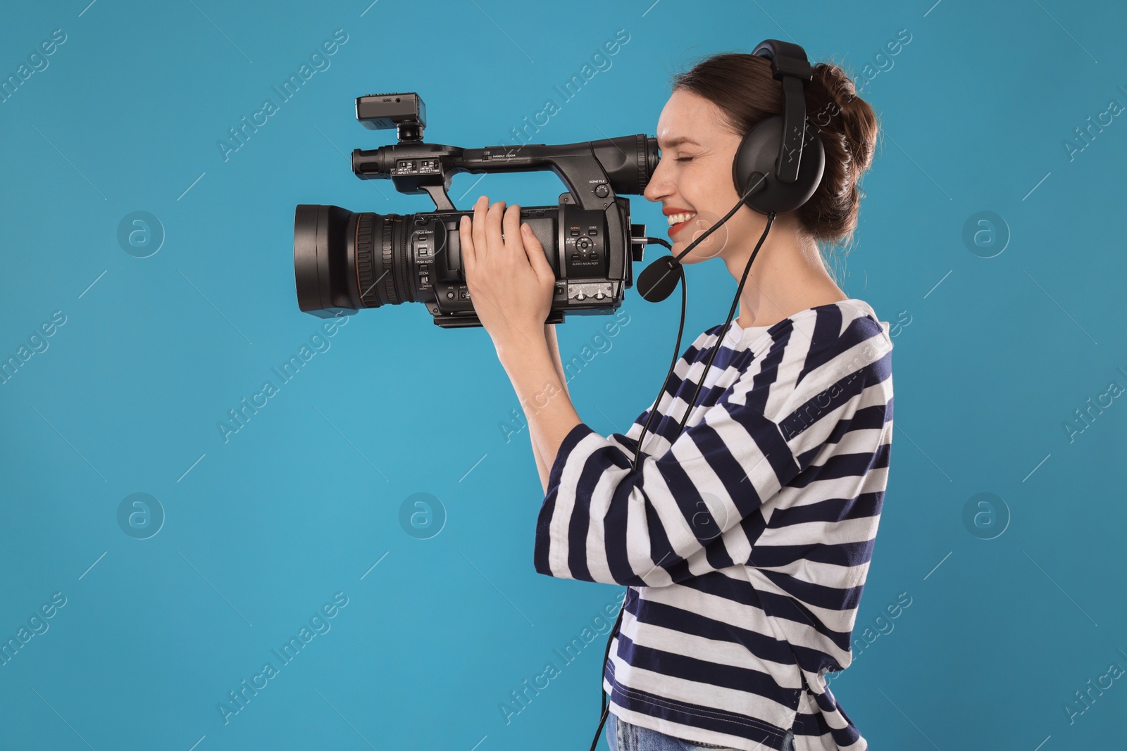 Photo of Happy woman with professional video camera and headset on light blue background