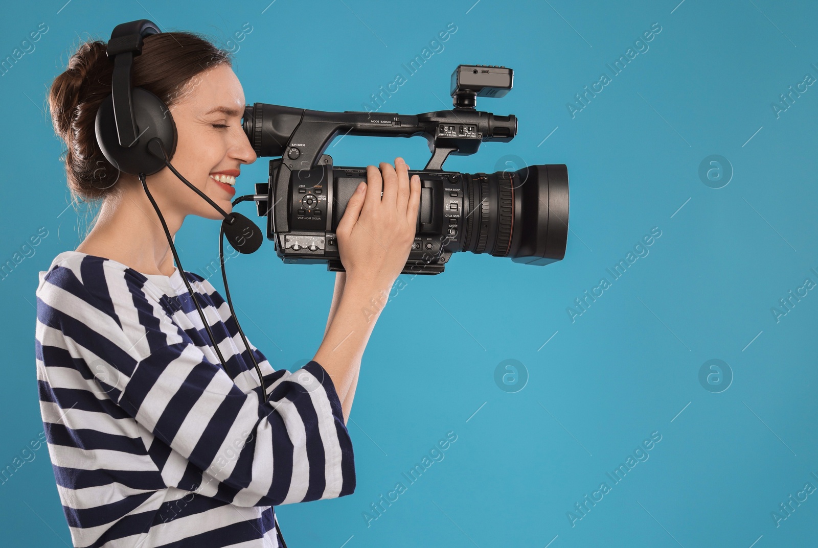 Photo of Happy woman with professional video camera and headset on light blue background, space for text