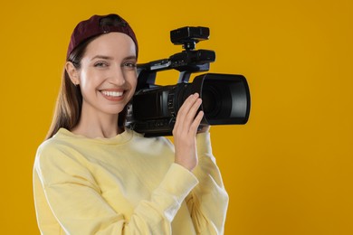 Photo of Happy woman with professional video camera on orange background, space for text