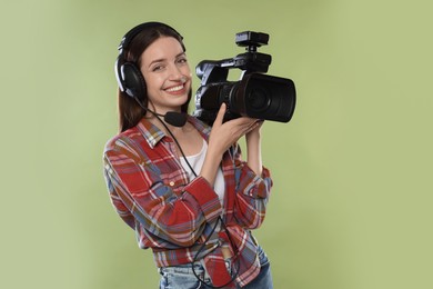 Photo of Happy woman with professional video camera and headset on pale olive background