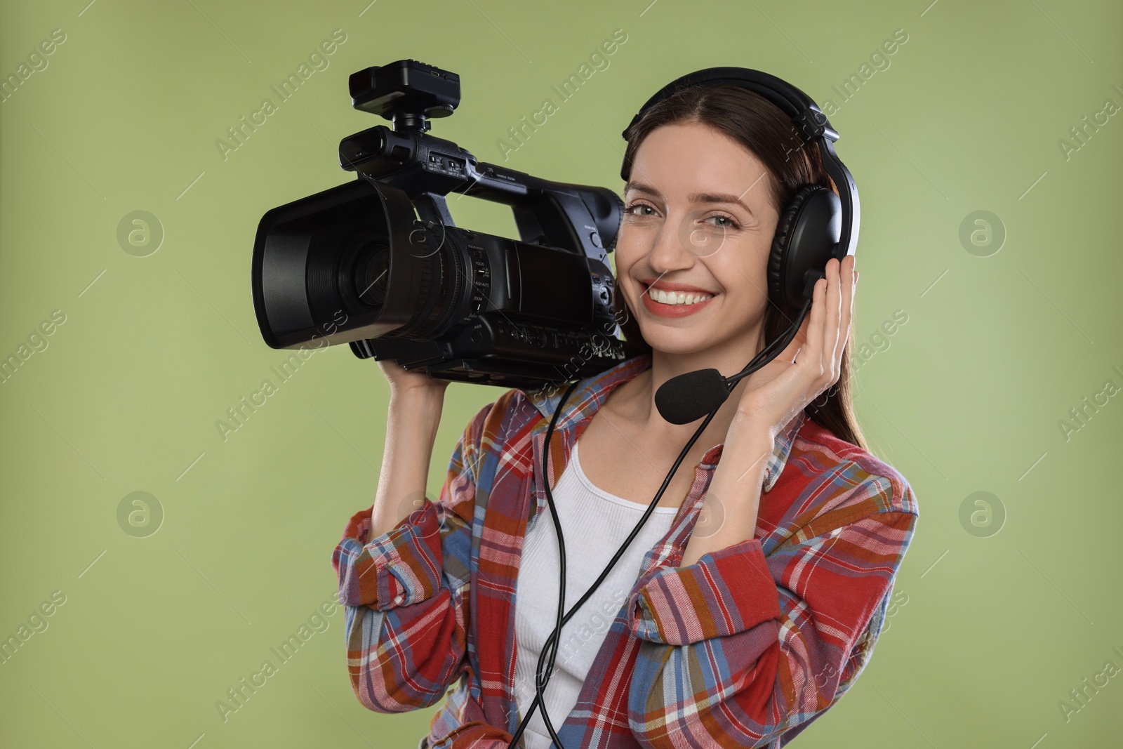 Photo of Happy woman with professional video camera and headset on pale olive background