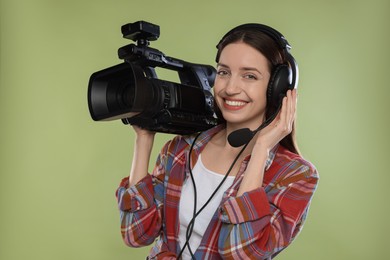 Photo of Happy woman with professional video camera and headset on pale olive background