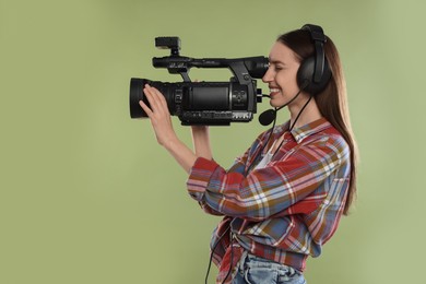 Photo of Happy woman with professional video camera and headset on pale olive background