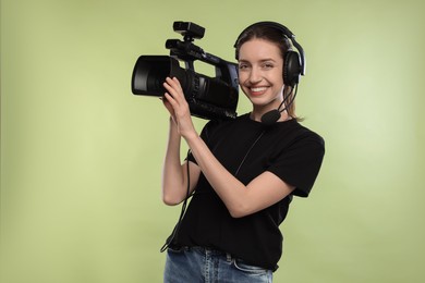 Photo of Happy woman with professional video camera and headset on pale olive background