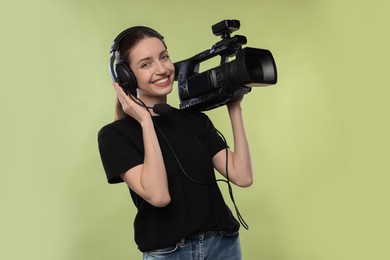 Photo of Happy woman with professional video camera and headset on pale olive background