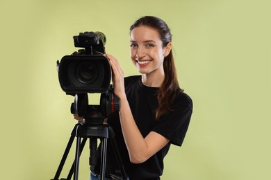 Photo of Happy woman with professional video camera on pale olive background