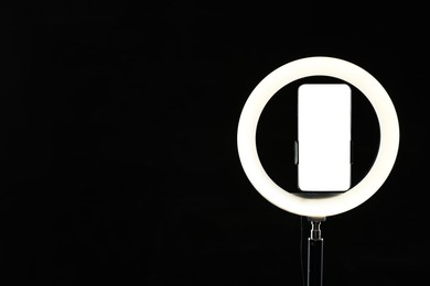 Photo of Ring lamp with smartphone on black background, space for text