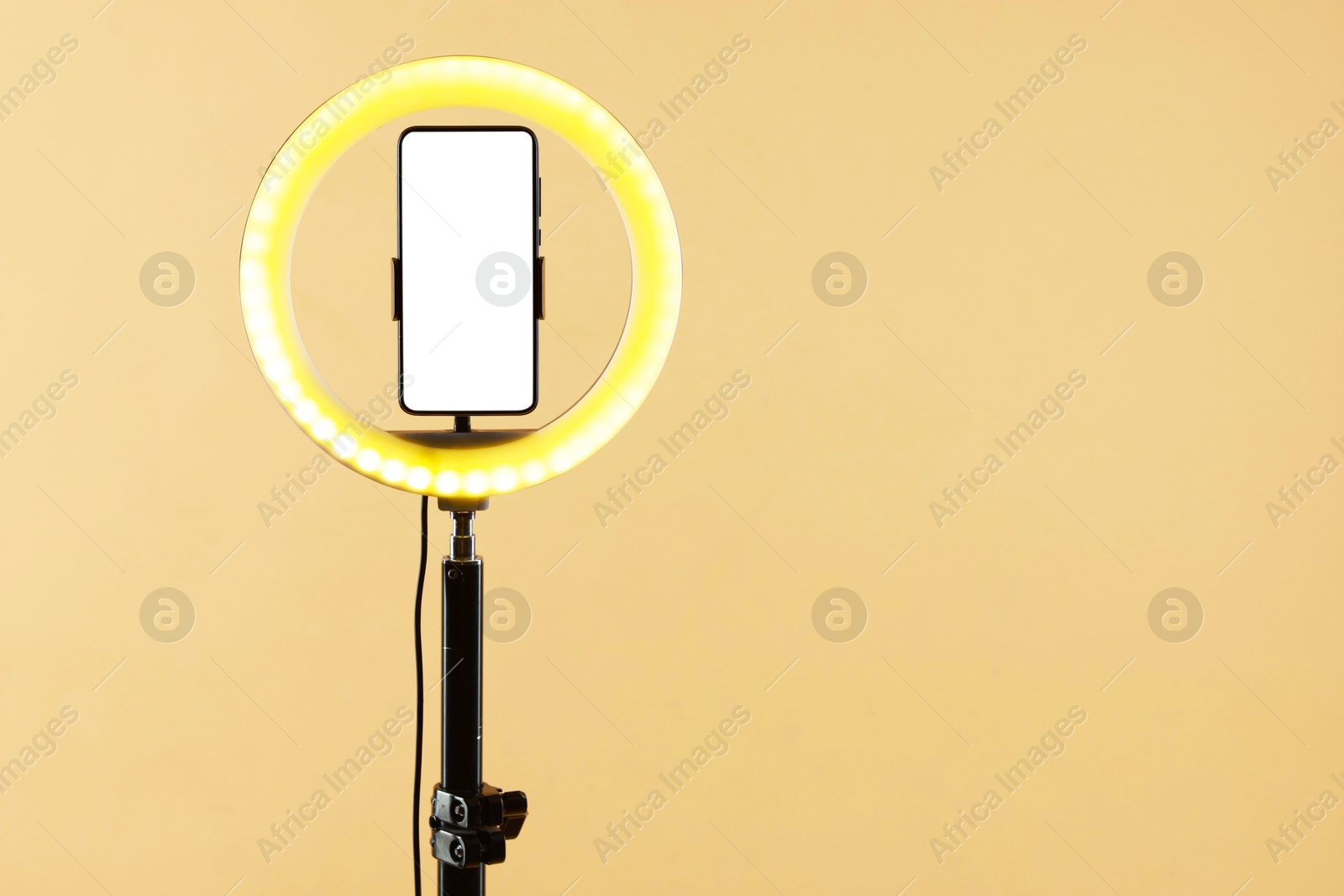 Photo of Ring lamp with smartphone on beige background, space for text